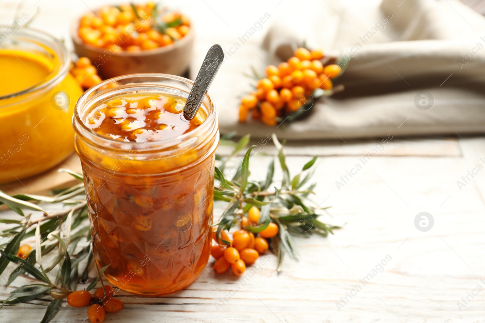 Photo of Delicious sea buckthorn jam and fresh berries on white wooden table. Space for text