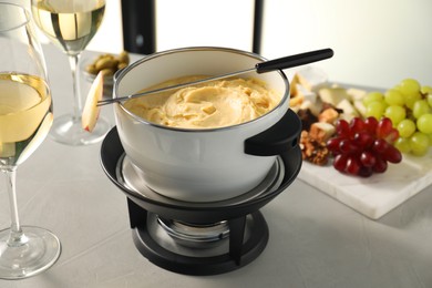 Photo of Fork with piece of apple, melted cheese in fondue pot, wine and products on grey table, closeup