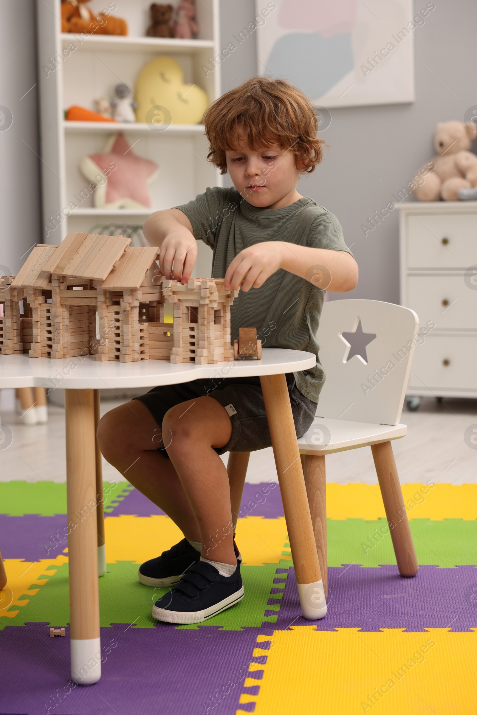 Photo of Little boy playing with wooden entry gate at white table in room. Child's toy