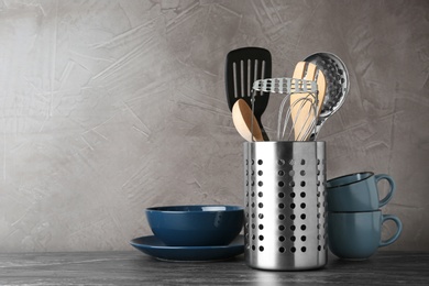 Photo of Holder with kitchen utensils on grey table against grey stone background. Space for text