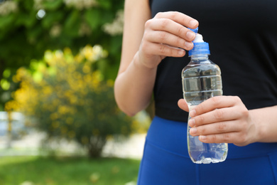 Photo of Young woman with bottle of pure water outdoors, closeup