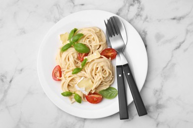 Photo of Delicious pasta with brie cheese, tomatoes, basil and cutlery on white marble table, top view