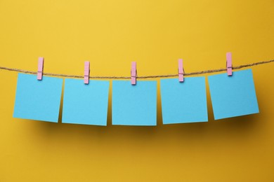 Photo of Wooden clothespins with blank notepapers on twine against yellow background. Space for text