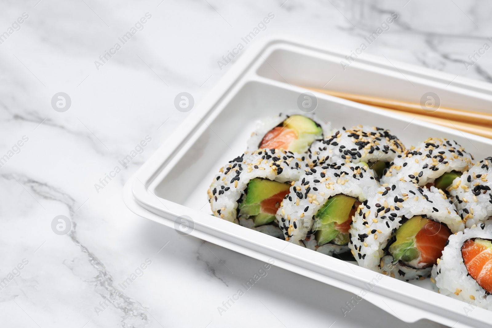 Photo of Food delivery. Delicious sushi rolls in plastic container on white marble table