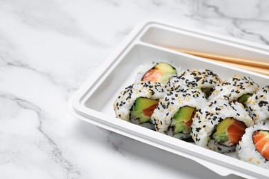 Photo of Food delivery. Delicious sushi rolls in plastic container on white marble table