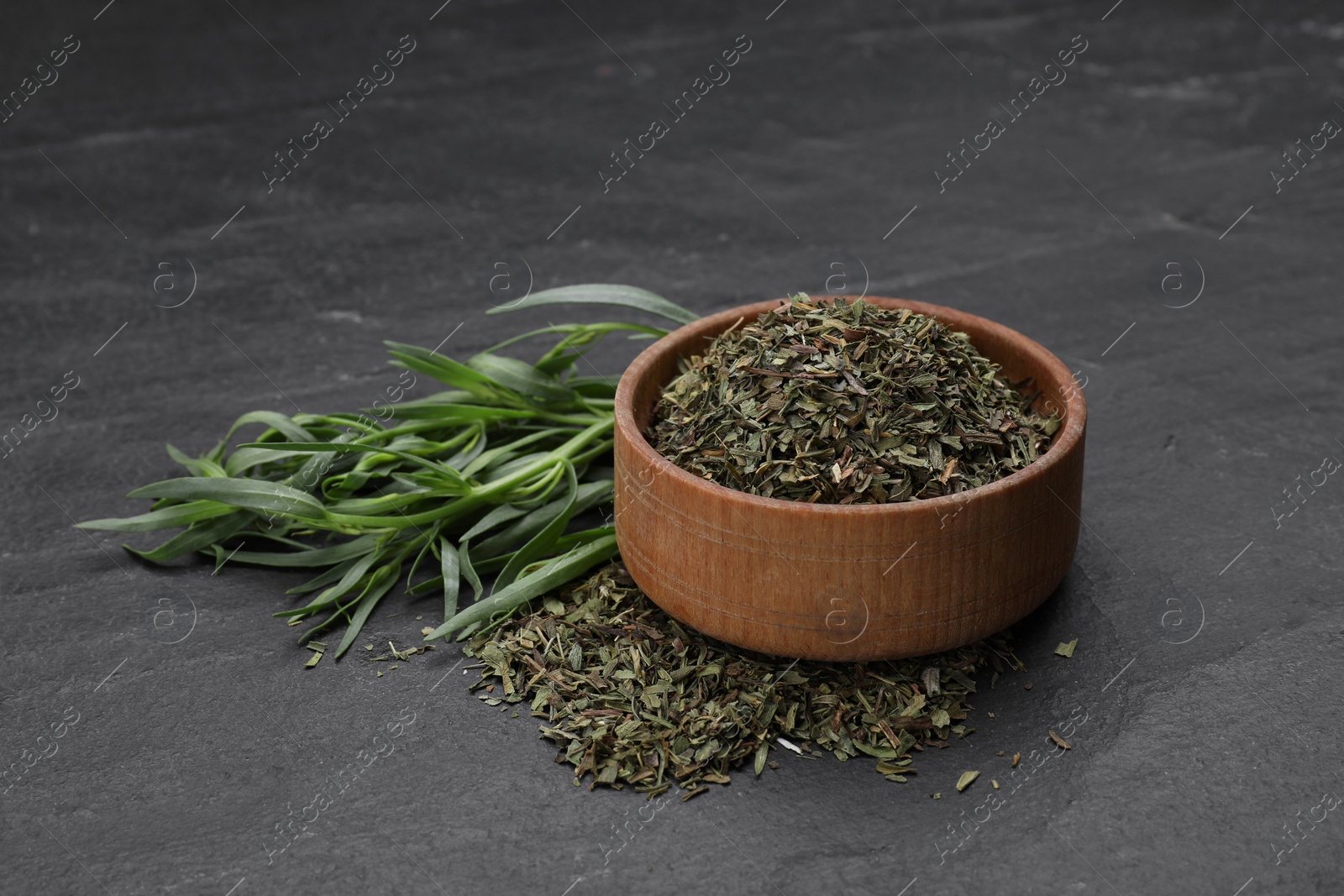 Photo of Dry and fresh tarragon on black textured table