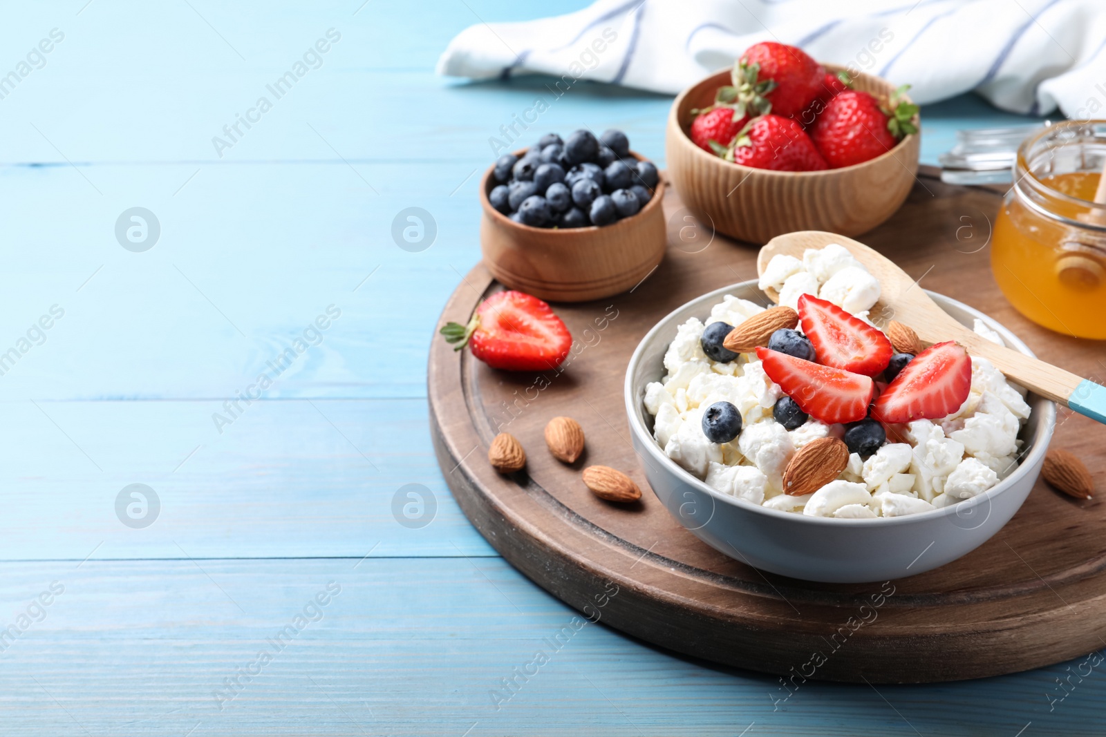 Photo of Bowl of fresh cottage cheese, berries with almond and ingredients on turquoise wooden table. Space for text