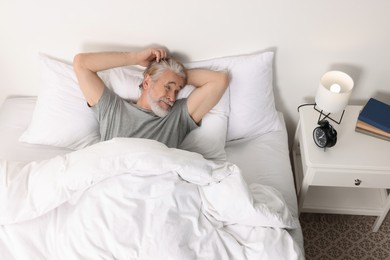 Senior man in bed and alarm clock on bedside table at home