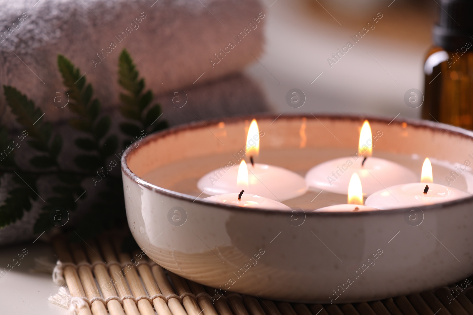 Photo of Spa composition. Burning candles in bowl, towels and fern leaf on table, closeup