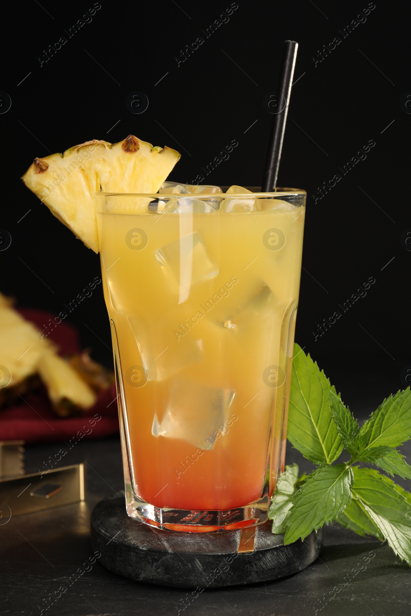 Photo of Glass of tasty pineapple cocktail and mint on black table