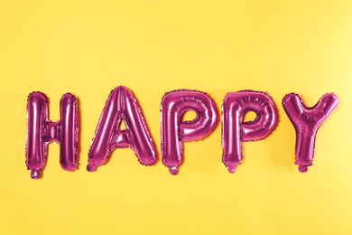 Word HAPPY made of pink foil balloons letters on yellow background