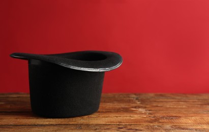 Photo of Magician's hat on wooden table against red background, space for text