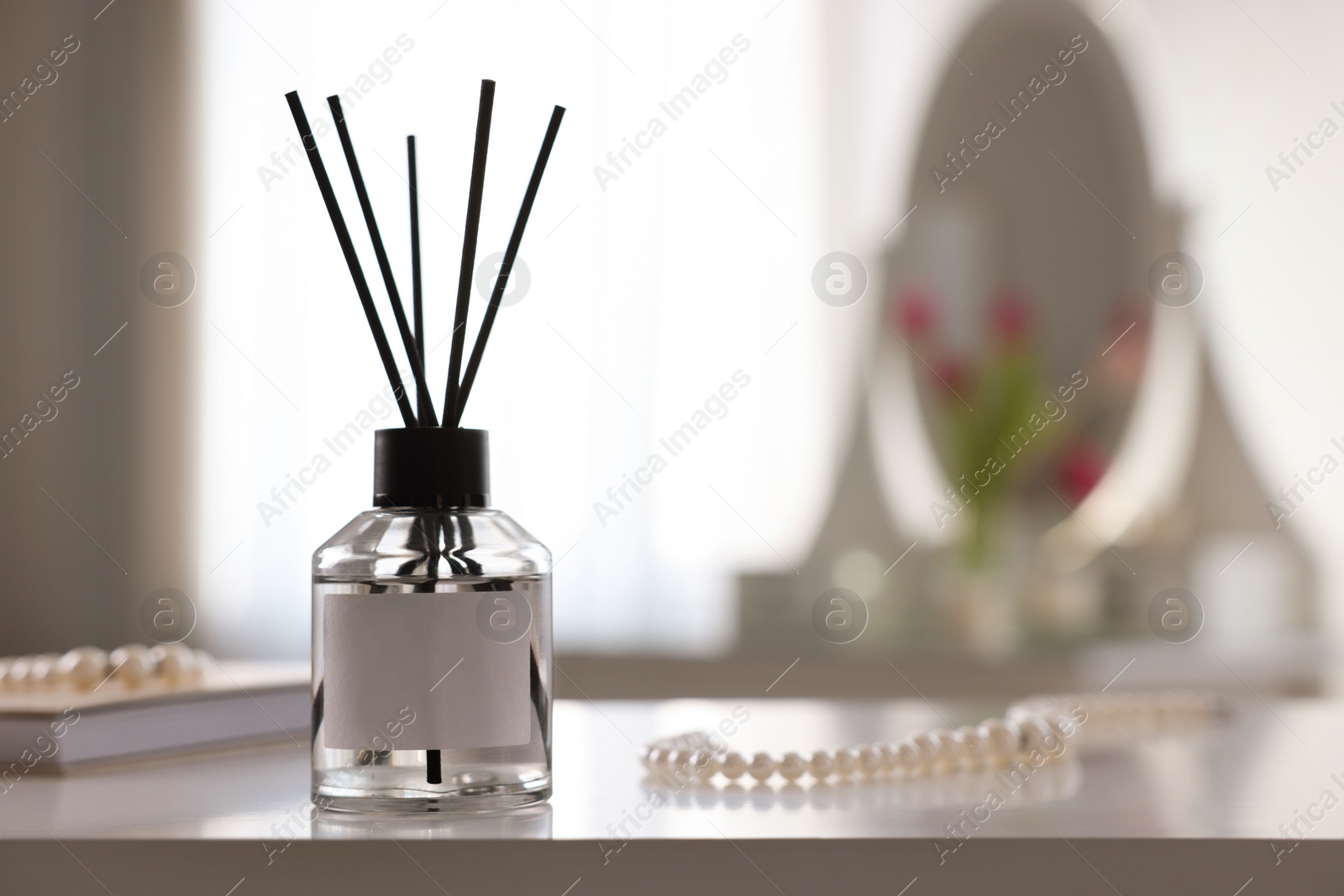 Photo of Reed diffuser and pearl necklace on white table indoors. Space for text