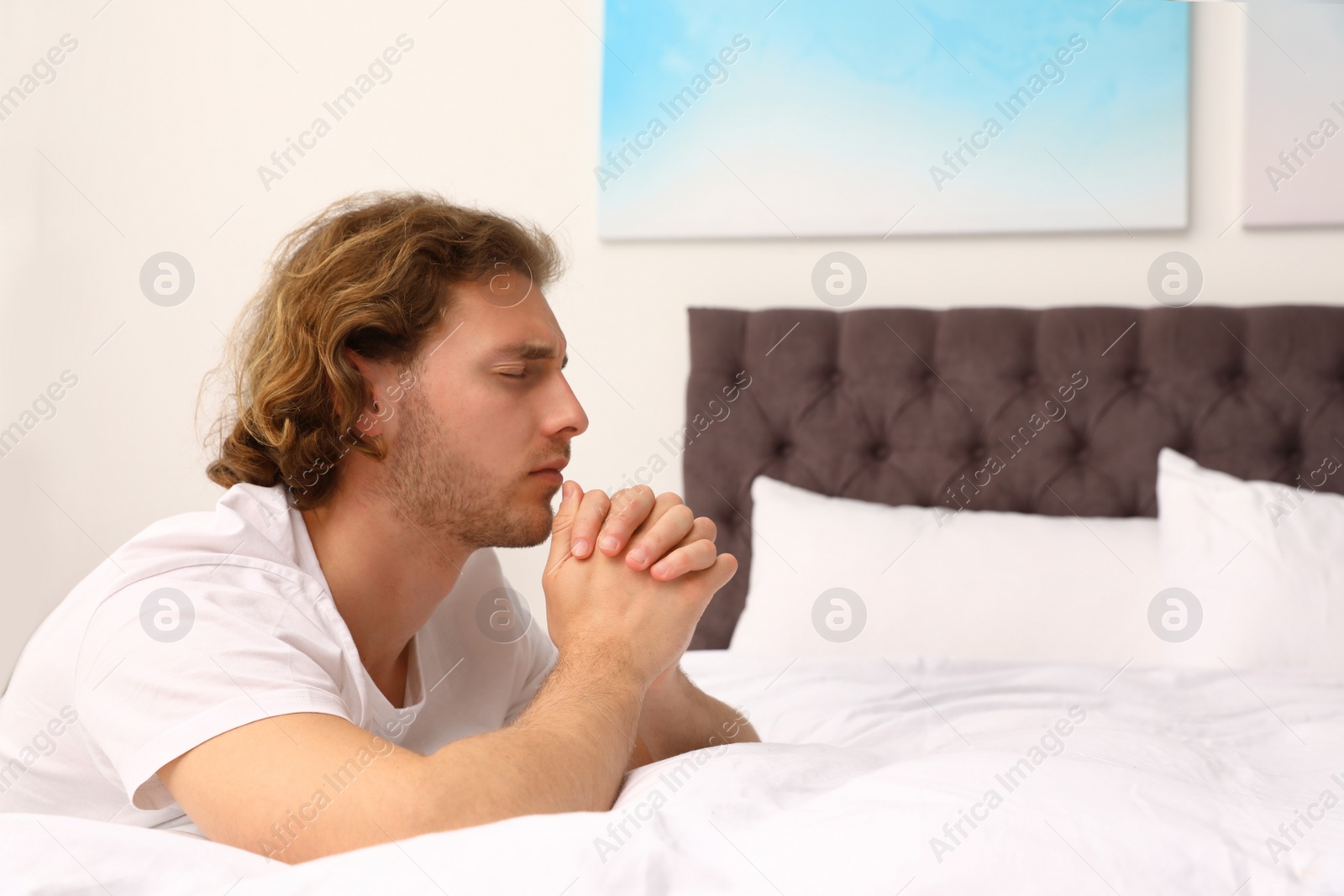 Photo of Handsome young man saying bedtime prayer at home. Space for text