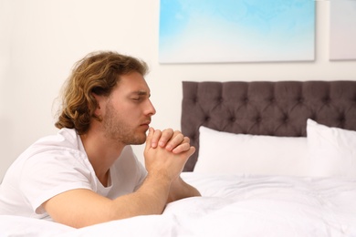 Photo of Handsome young man saying bedtime prayer at home. Space for text