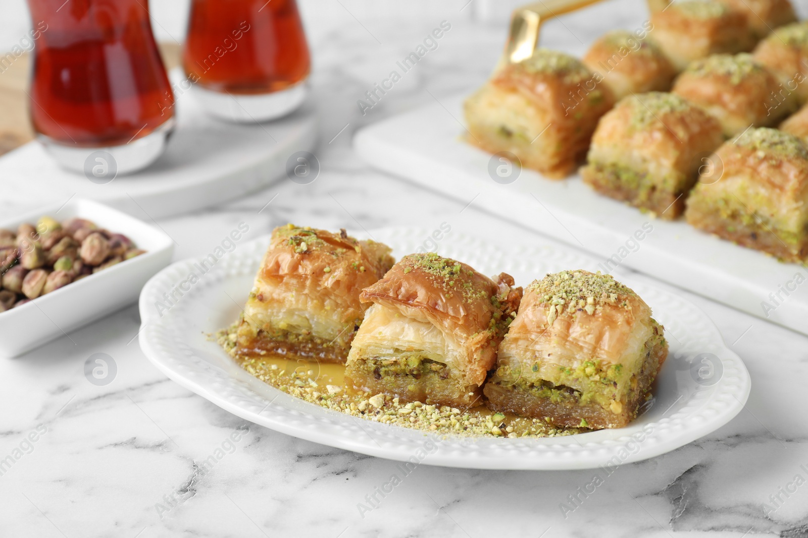 Photo of Delicious fresh baklava with chopped nuts and honey on white marble table, closeup. Eastern sweets