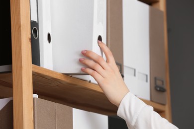 Woman taking folder with documents from shelf in office, closeup