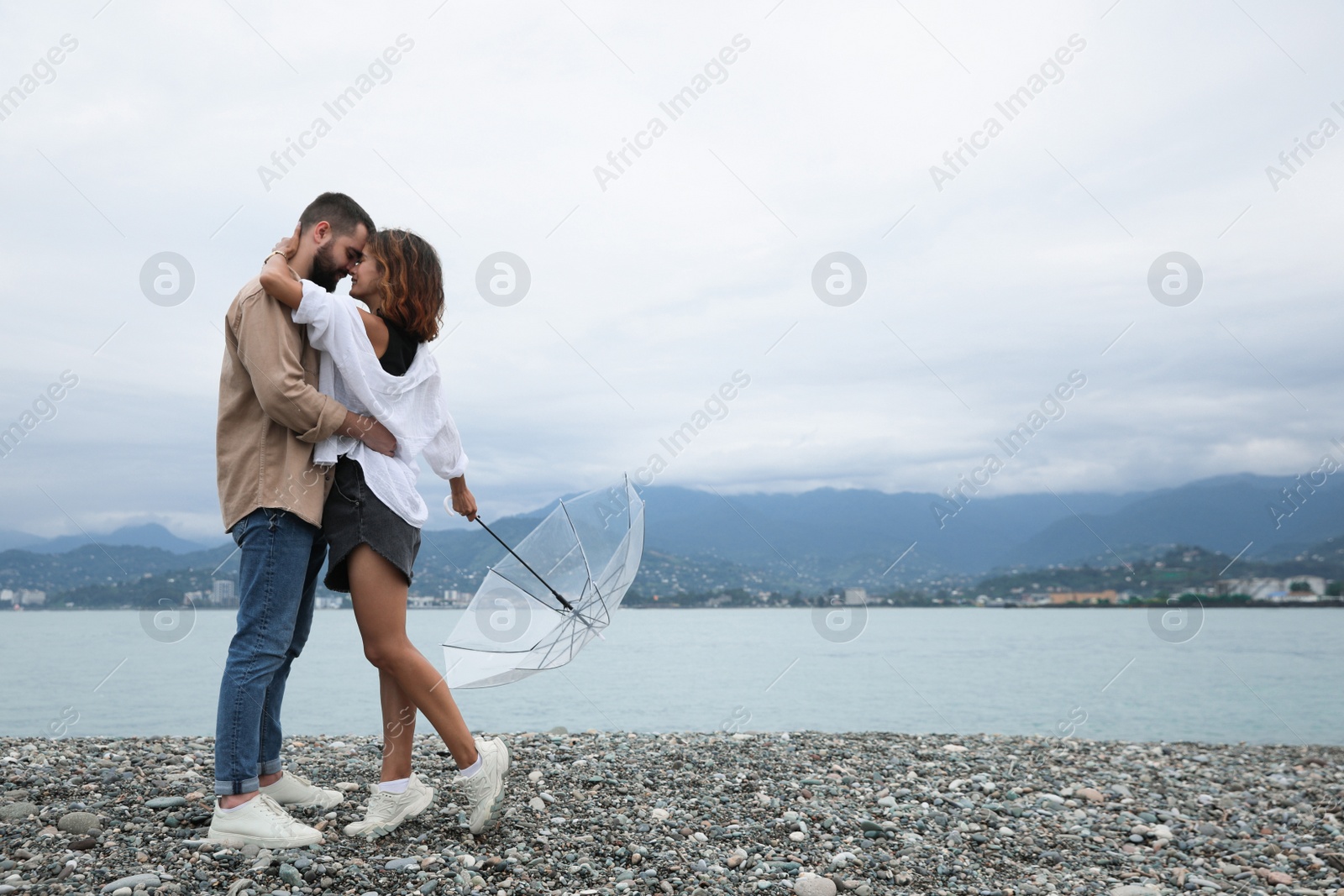 Photo of Young couple with umbrella enjoying time together under rain on beach, space for text