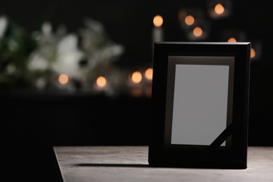 Photo of Funeral photo frame with black ribbon on table in dark room