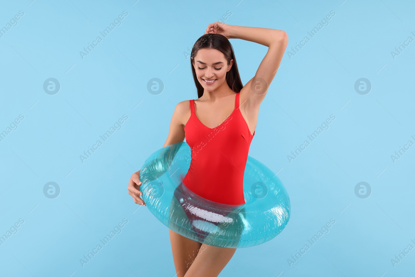 Photo of Young woman in stylish swimsuit with inflatable ring on light blue background