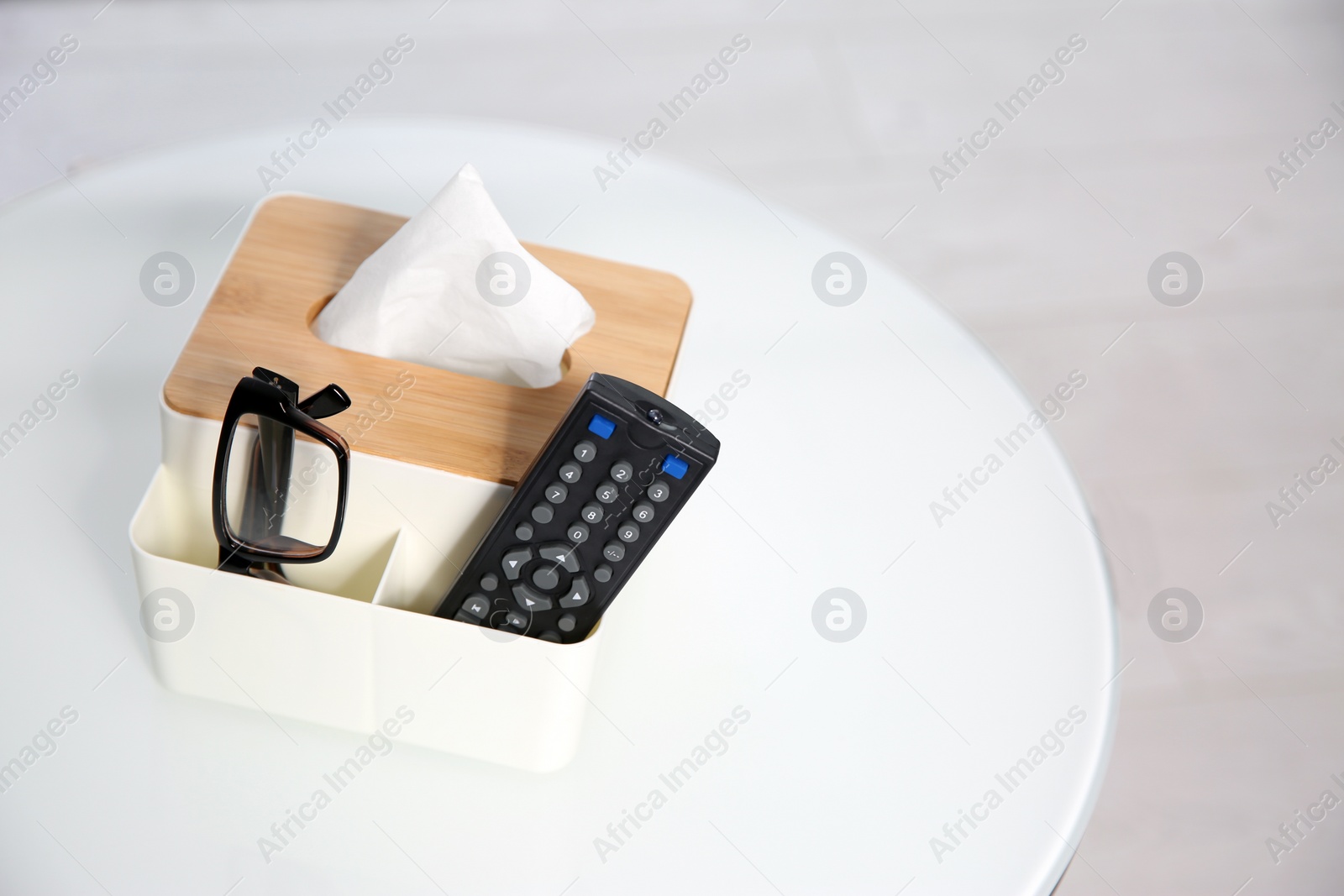 Photo of Box with paper tissues, glasses and TV remote control on white table. Space for text