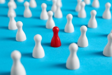 Photo of One red pawn among others on light blue background, closeup. Social inclusion concept