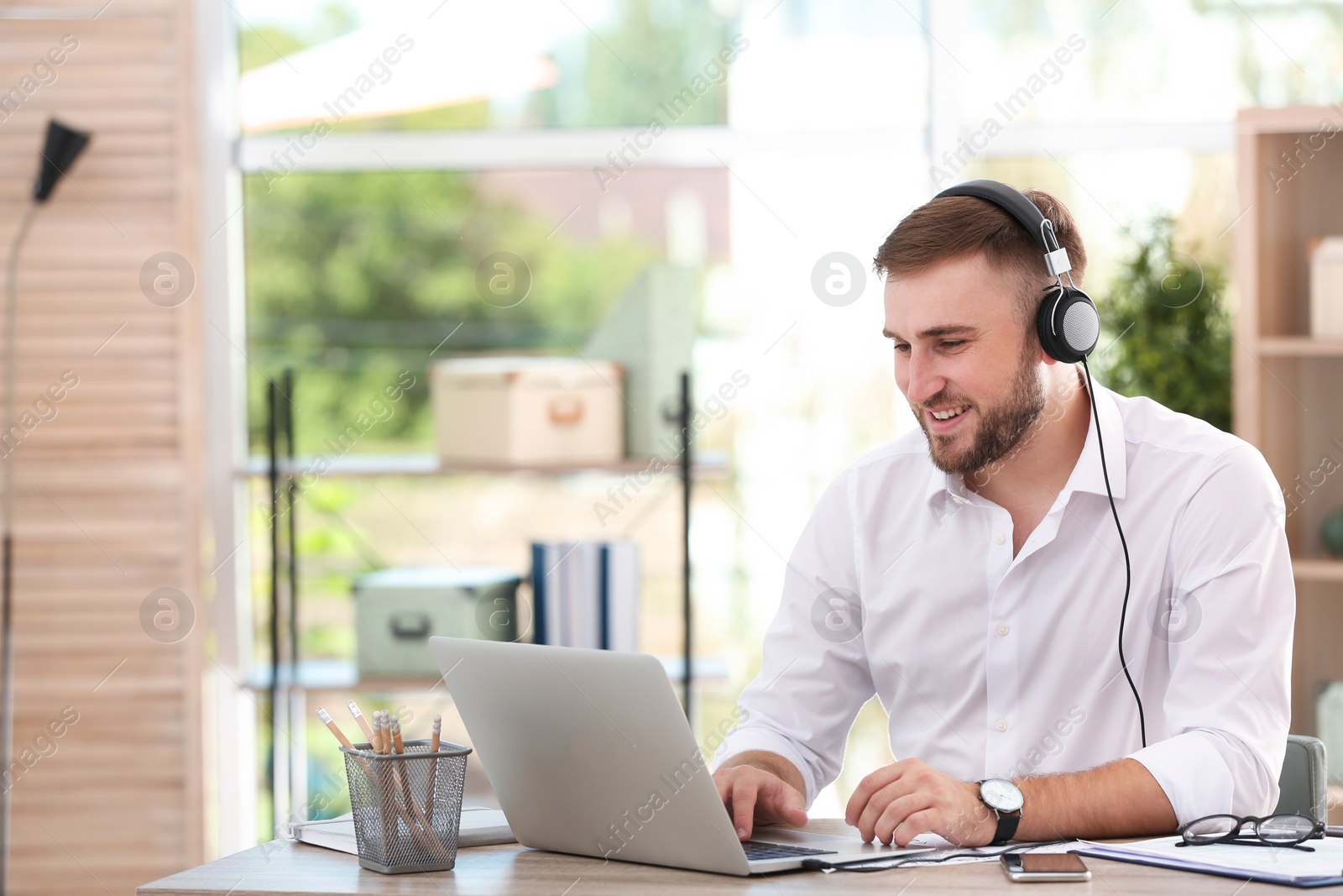 Photo of Young businessman using laptop and listening to music at table in office