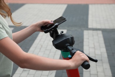 Woman riding modern electric kick scooter while using smartphone outdoors