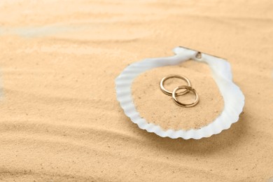 Honeymoon concept. Two golden rings and shell on sand