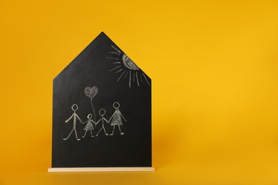 Photo of Chalk drawing of parents with their children on house shaped blackboard against orange background, space for text. Family Day