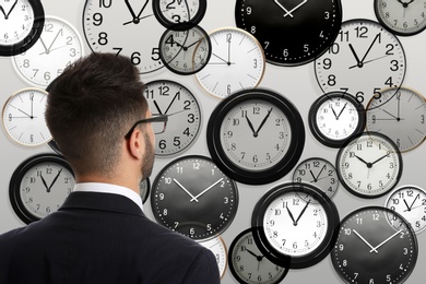 Image of Time management concept. Businessman standing in front of different clocks on light background