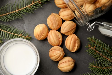 Photo of Homemade walnut shaped cookies, milk and fir branches on black table, flat lay