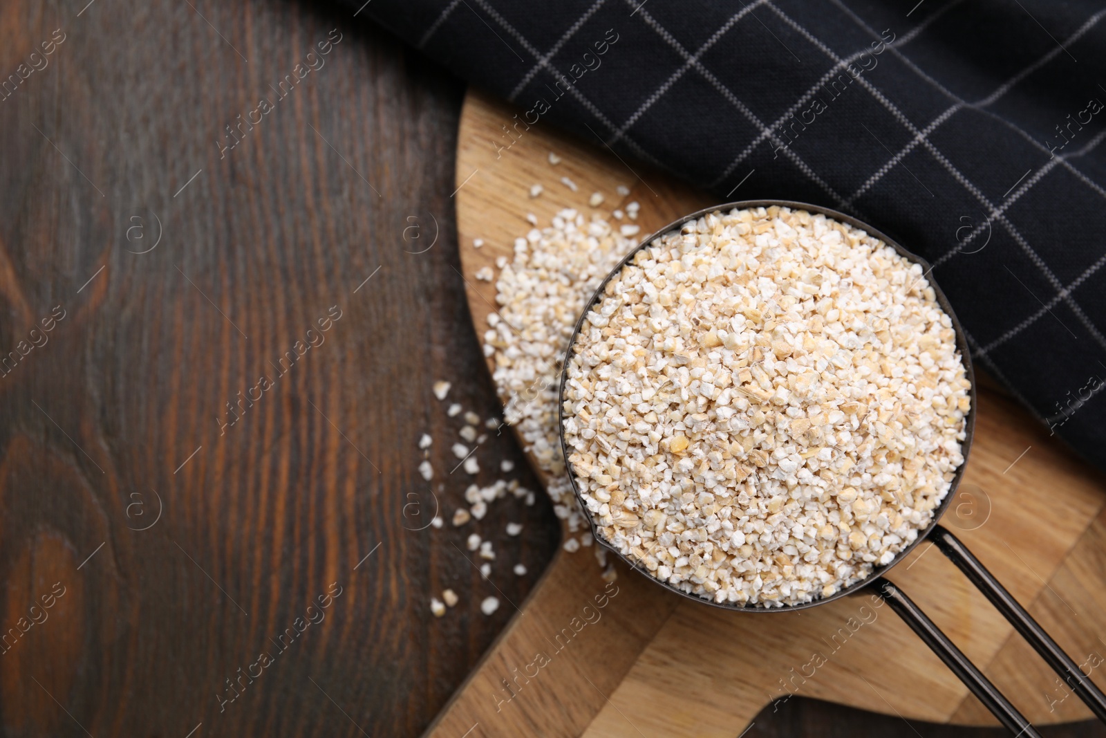 Photo of Raw barley groats in scoop on wooden table, top view. Space for text