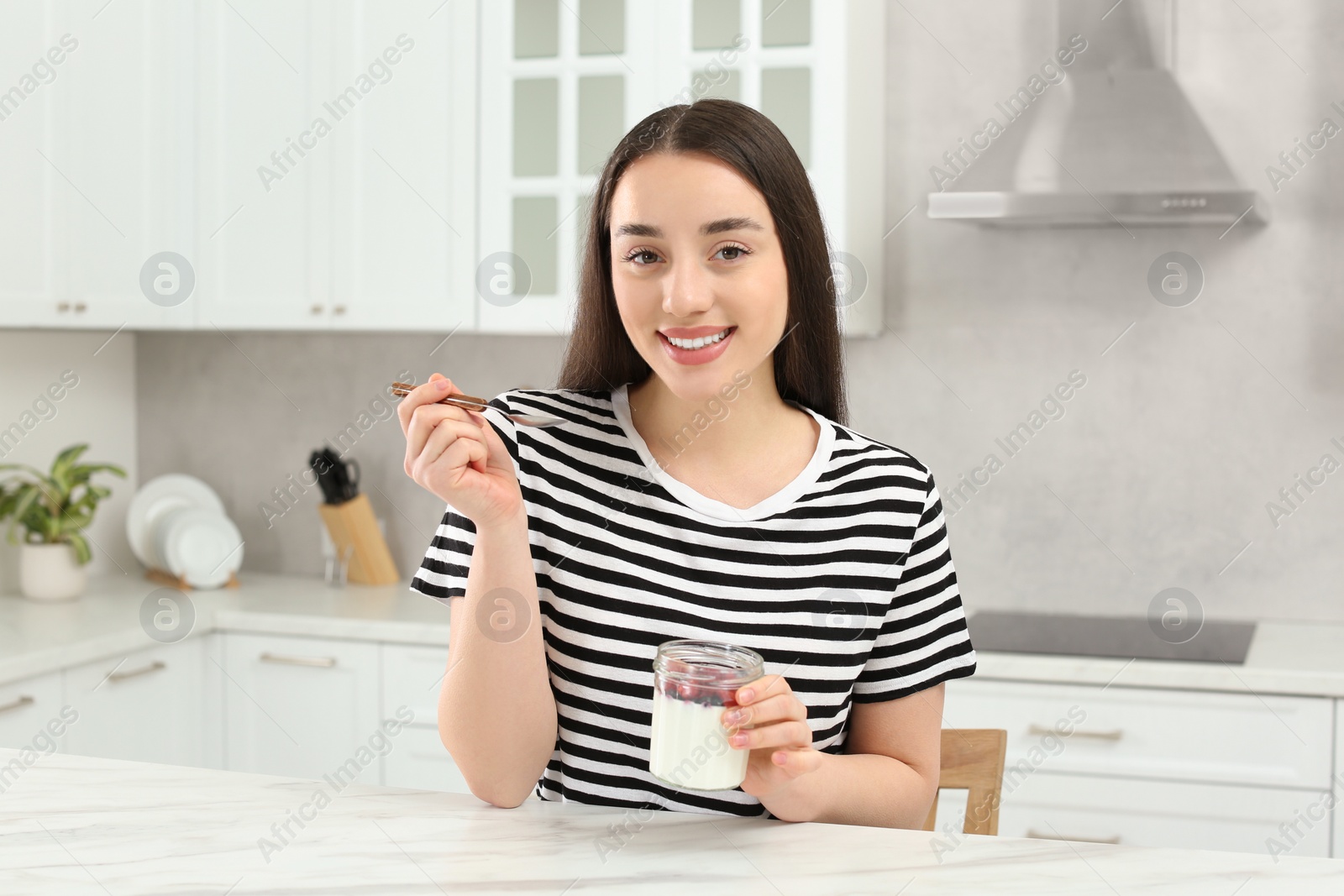 Photo of Portrait of happy woman with tasty yogurt in kitchen