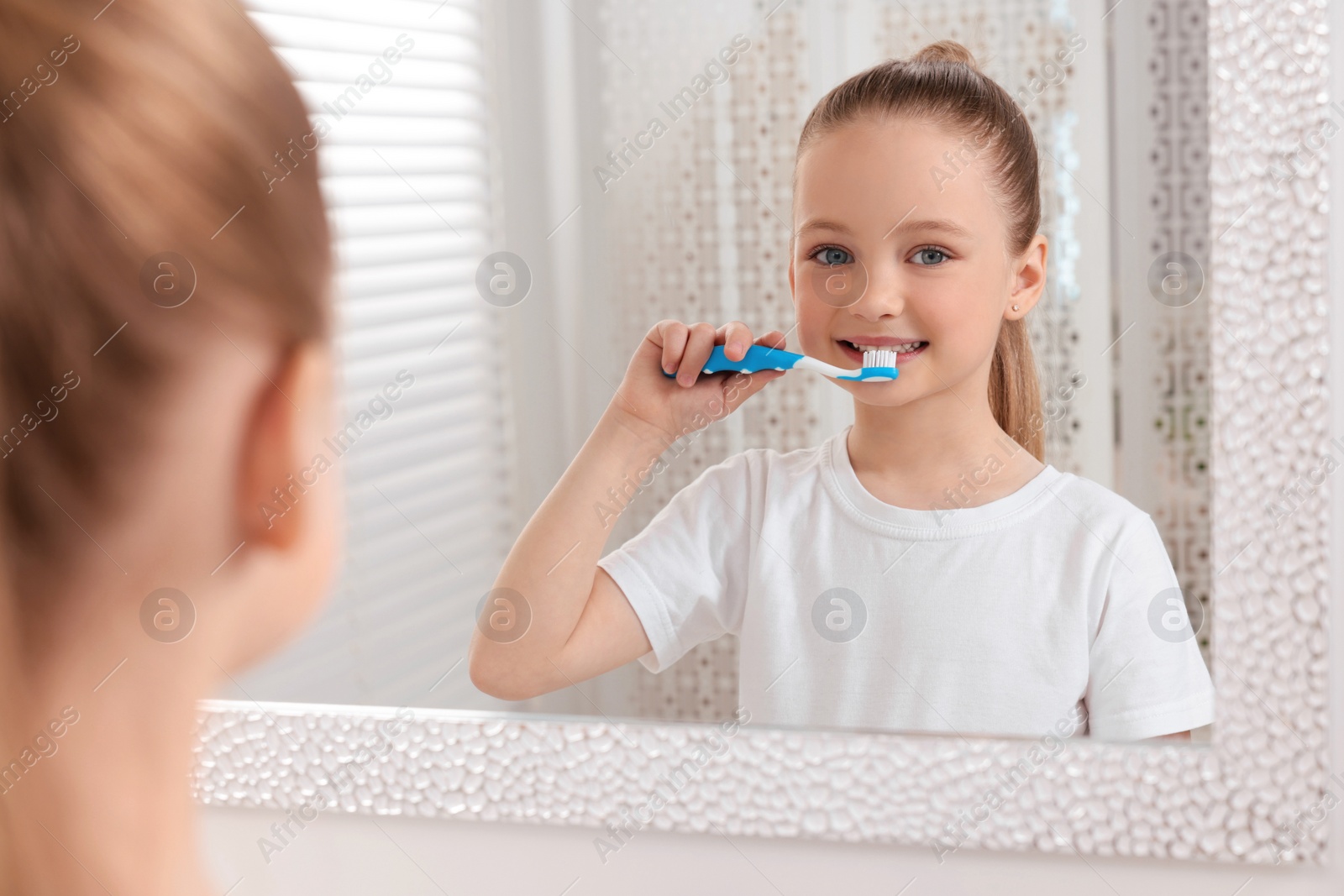 Photo of Cute little girl brushing her teeth with plastic toothbrush near mirror in bathroom