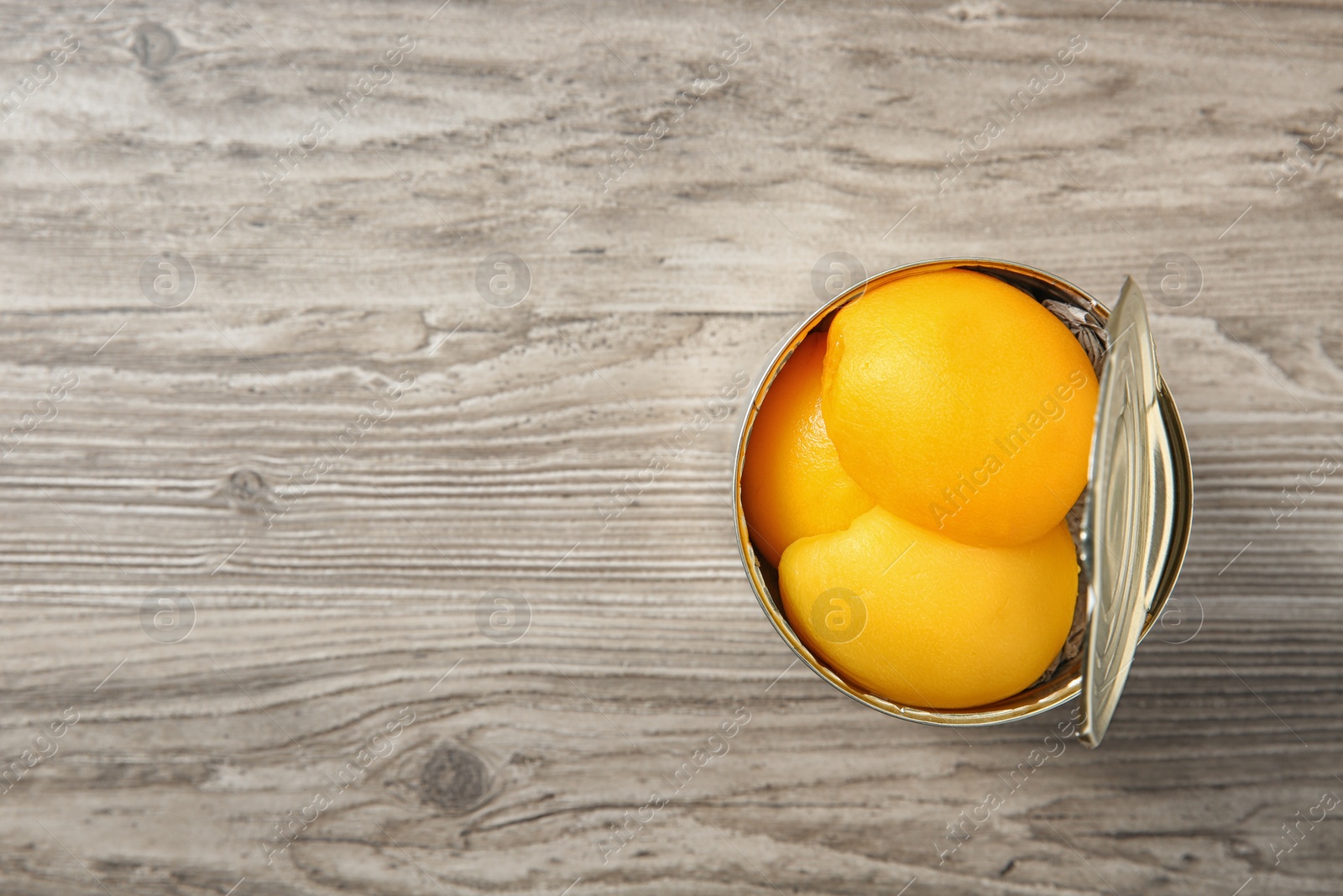 Photo of Open tin can of peaches on wooden background, top view. Space for text