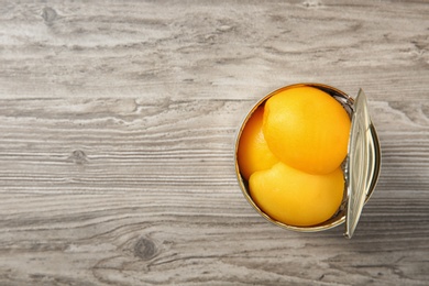 Photo of Open tin can of peaches on wooden background, top view. Space for text