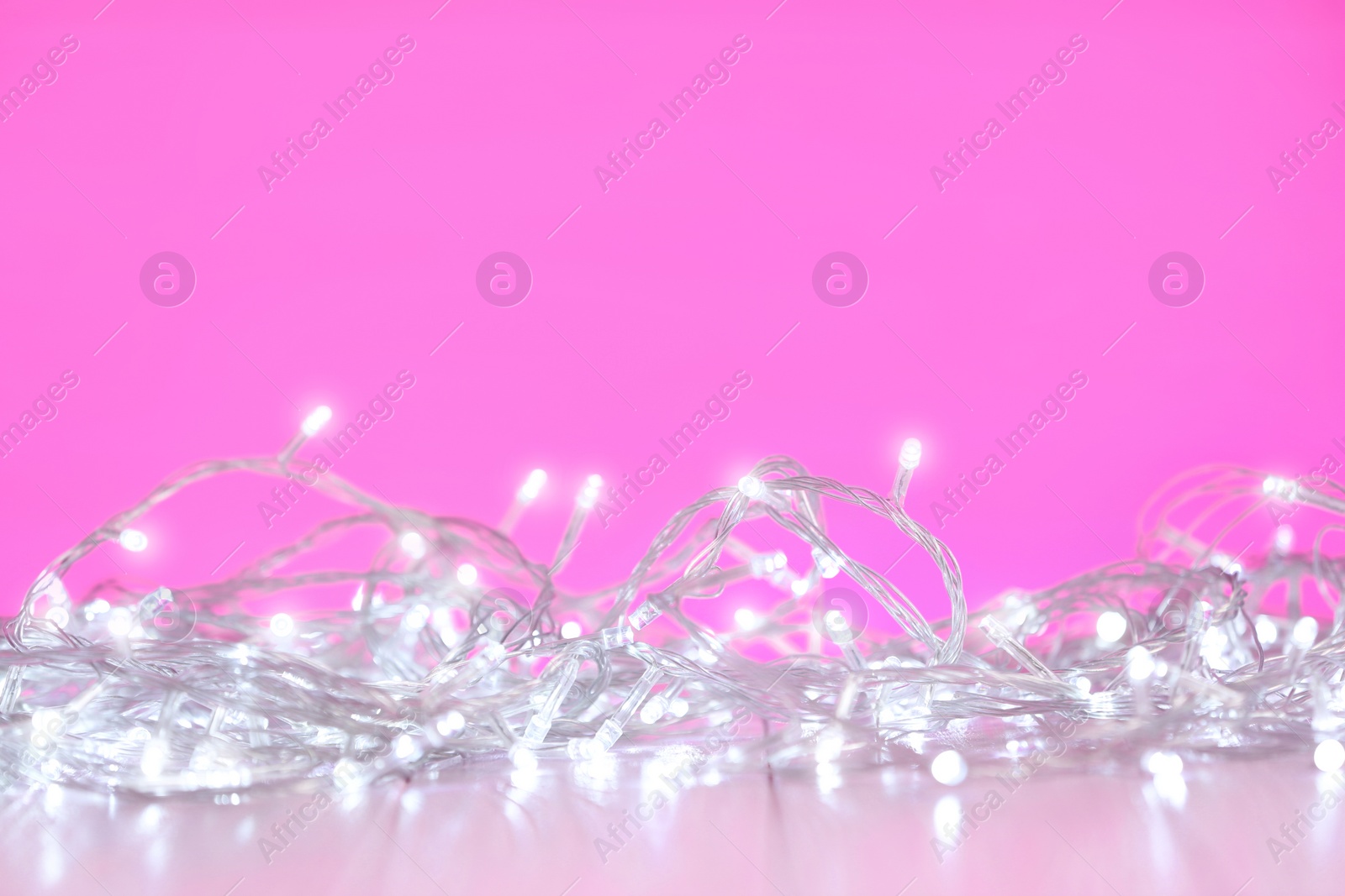 Photo of White Christmas lights on wooden table against pink background