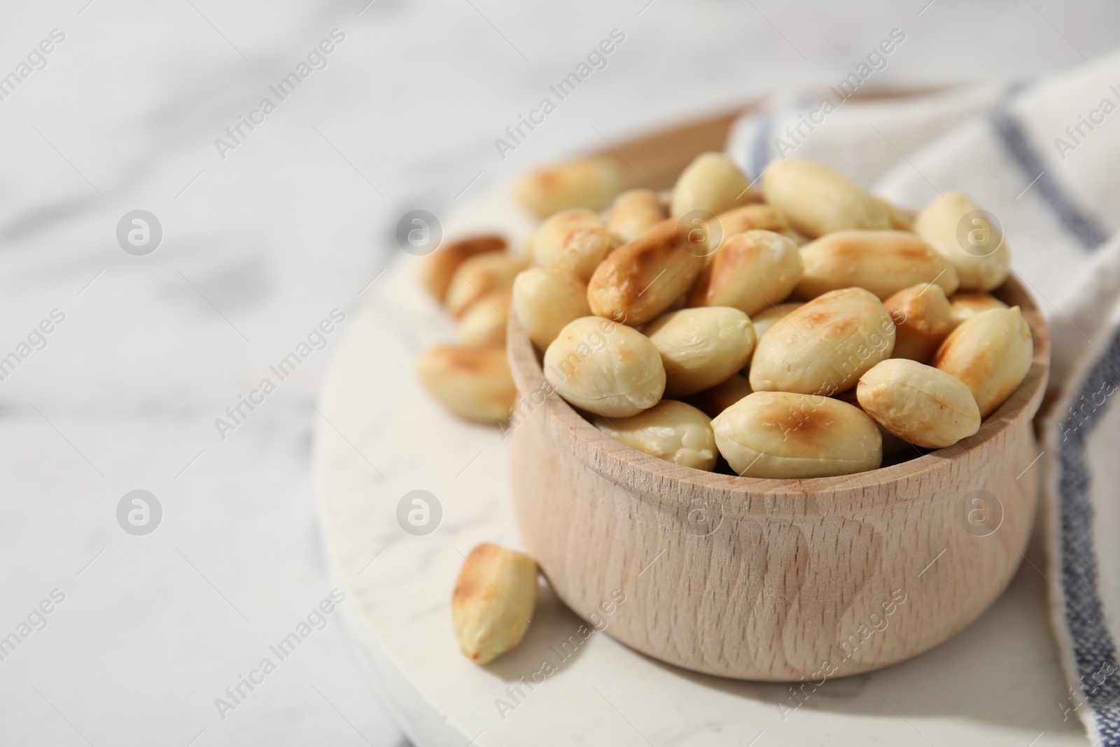 Photo of Roasted peanuts in bowl on white table, closeup. Space for text