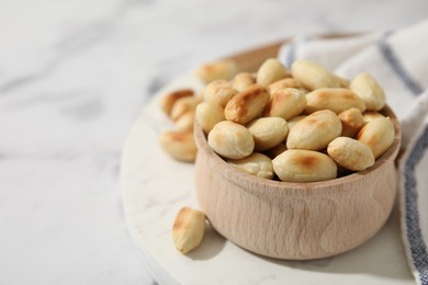 Photo of Roasted peanuts in bowl on white table, closeup. Space for text