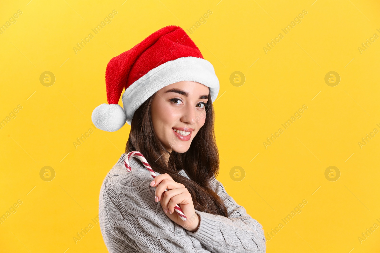 Photo of Beautiful woman in Santa Claus hat holding candy cane on yellow background