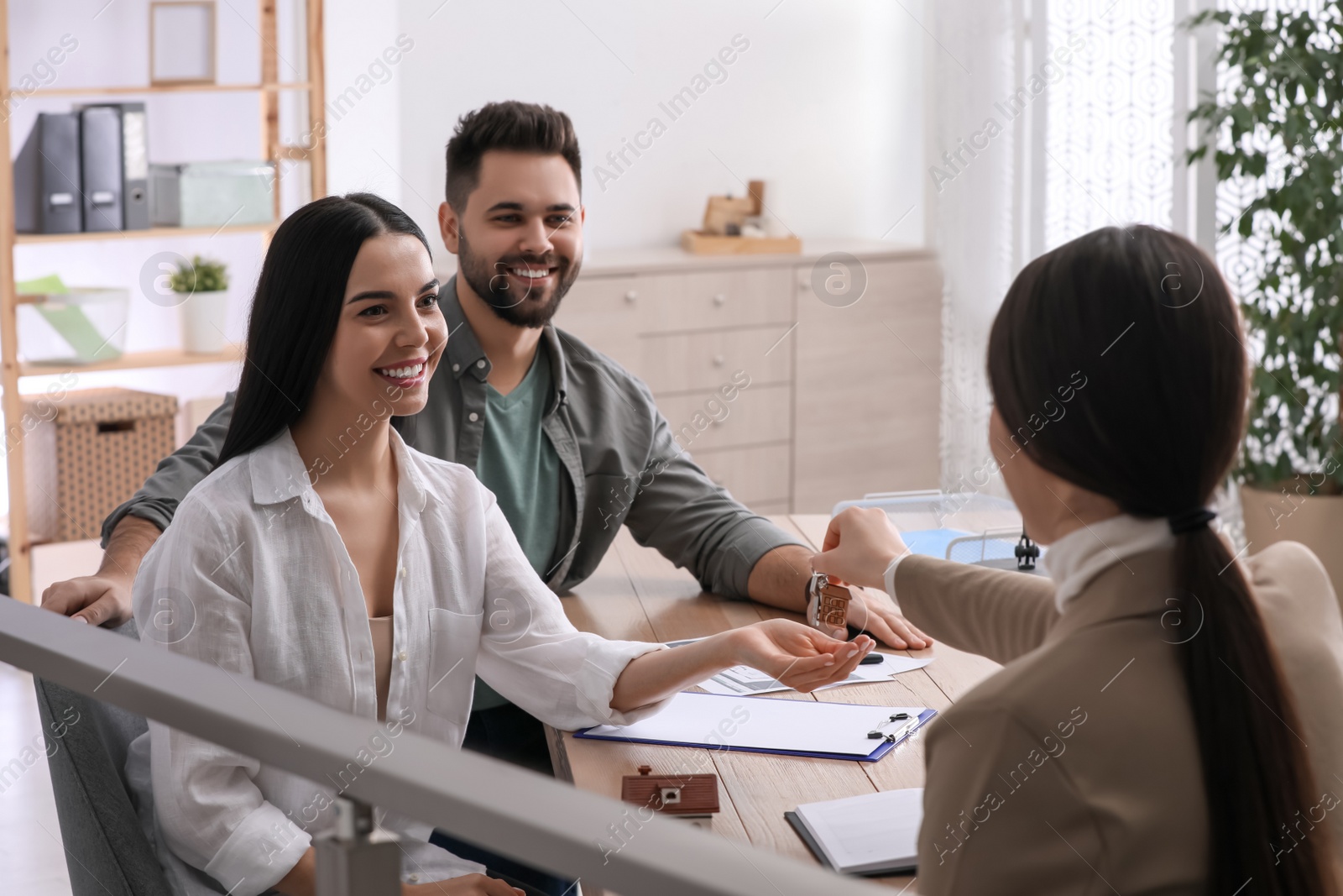 Photo of Real estate agent giving house key to young couple in office. Mortgage concept