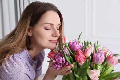 Photo of Woman smelling bouquet of beautiful tulips indoors