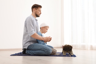 Photo of Muslim man and his son praying together indoors. Space for text