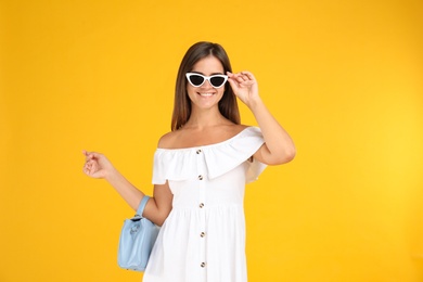 Young woman wearing stylish white dress with elegant bag on yellow background