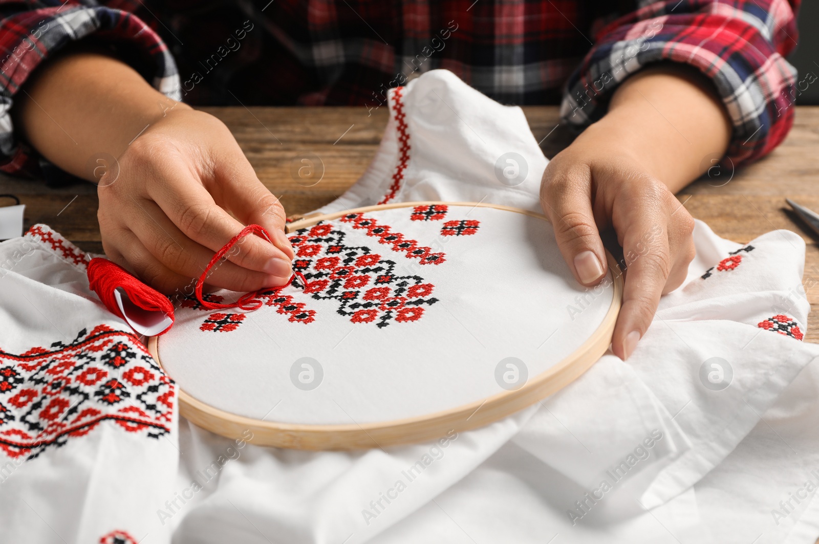 Photo of Woman embroidering white shirt with colorful threads at wooden table, closeup. Ukrainian national clothes