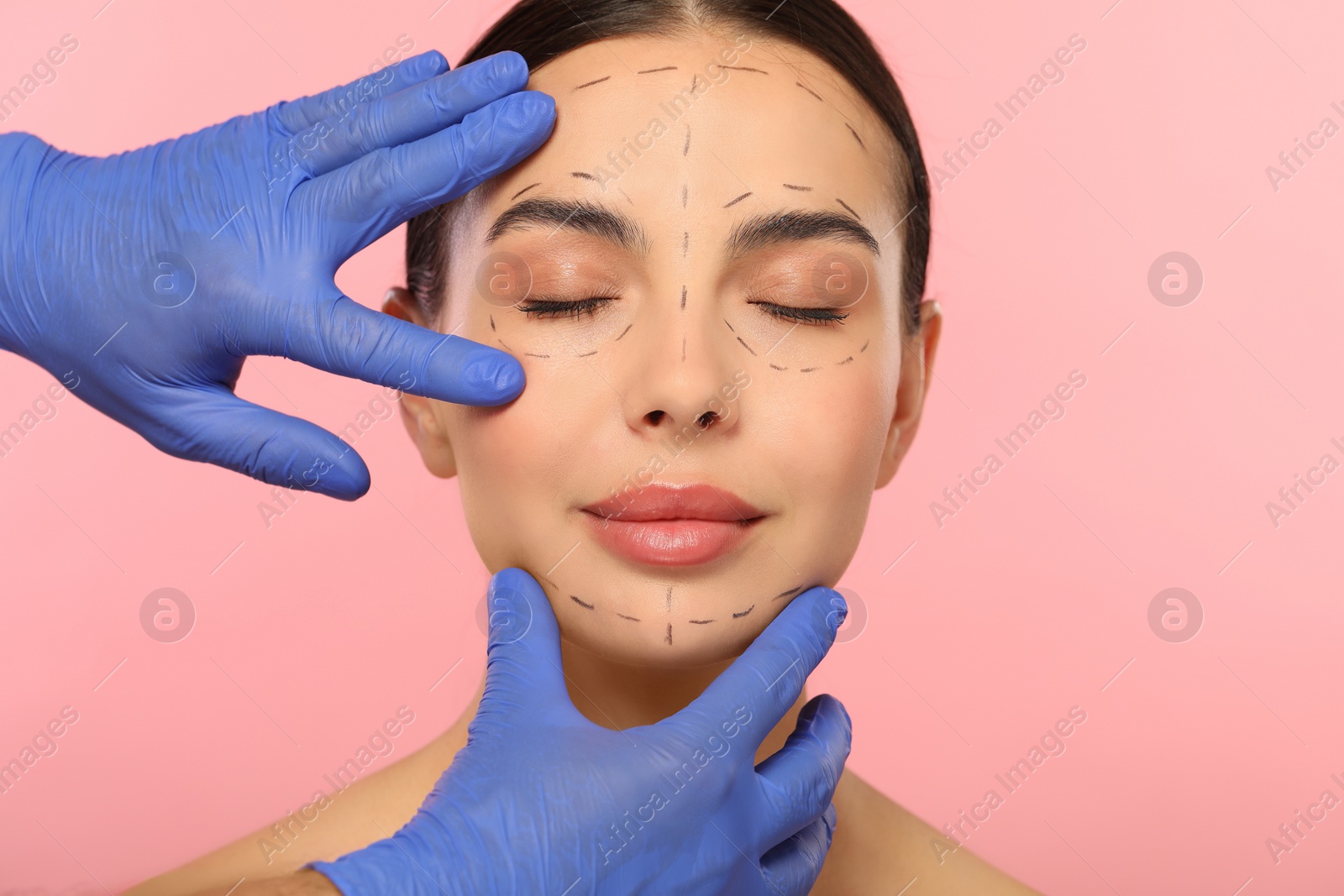 Photo of Doctor checking patient's face before cosmetic surgery operation on pink background, closeup