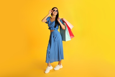 Photo of Beautiful young woman with paper shopping bags on yellow background