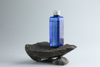 Bottle of cosmetic product on stones against light grey background