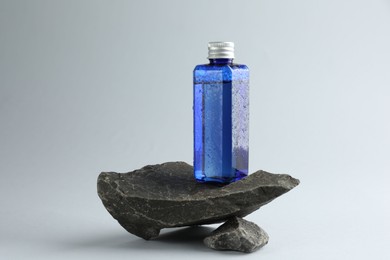 Photo of Bottle of cosmetic product on stones against light grey background